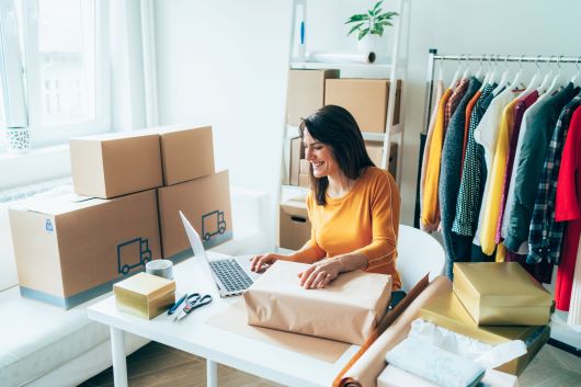 Woman on computer surrounded by boxes and rack of clothes