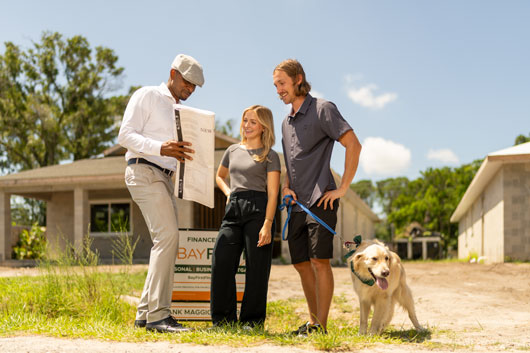 Contratista mostrando planos de una casa a una pareja paseando un perro