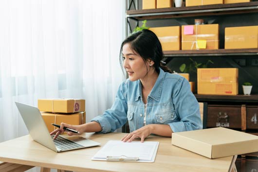 Mujer usando una computadora portátil frente a estantes llenos de cajas